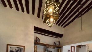 A room with wooden beams on the ceiling, a hanging light fixture, a reception sign, framed pictures, and a mirror. - Stone Town House (Zanzibar Town)
