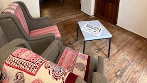 A room with a wooden ceiling, a bed with a white headboard, a small table with a newspaper, and a patterned throw on the sofa. - Stone Town House (Zanzibar Town)