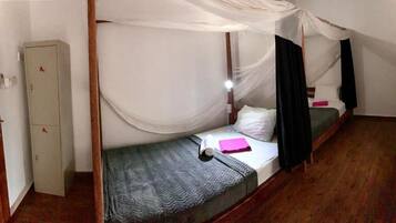A single bed with a mosquito net, a small cabinet, and a wooden floor.
