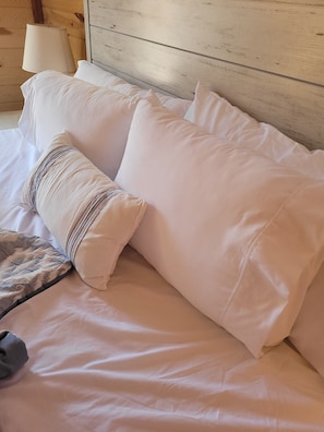 Un letto con lenzuola e cuscini bianchi, una lampada e una testiera in legno.