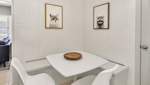 Ein kleiner Essbereich mit einem weißen Tisch und zwei weißen Stühlen. An der Wand hängen gerahmte Tierbilder.