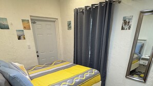 A bedroom with a bed, a bedside table, a mirror, and a door. - Cozy, comfortable 1-bedroom apartment in charming Eleuthera near to the beach. (North Eleuthera)