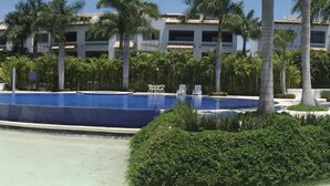 Ein Pool mit Liegestühlen, umgeben von Palmen und einem Gebäude mit einem Ziegeldach.