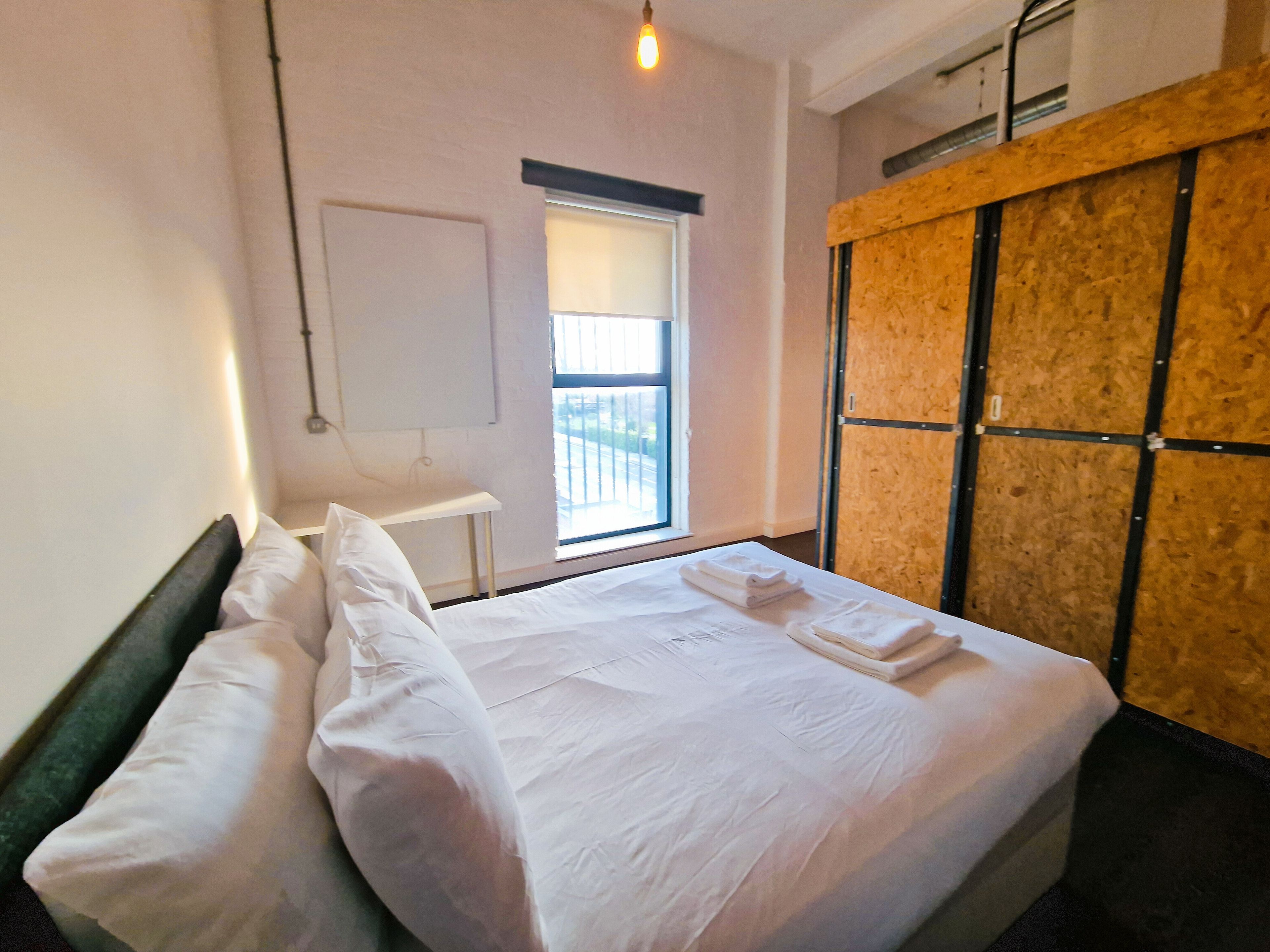 Een hotelkamer met een bed, een raam, een whiteboard en een wand van hout.