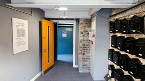 A hallway with a fire exit, a wall-mounted mailbox system, and a poster on the wall. - Modern Stylish Apartment near the City Centre (Liverpool)