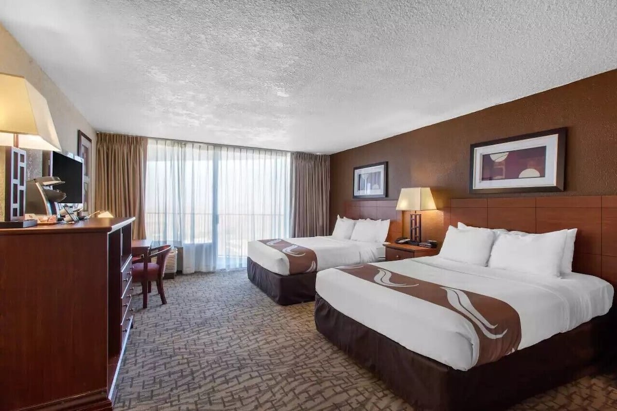 Una habitación de hotel con dos camas, un escritorio con lámpara, una silla y un televisor.