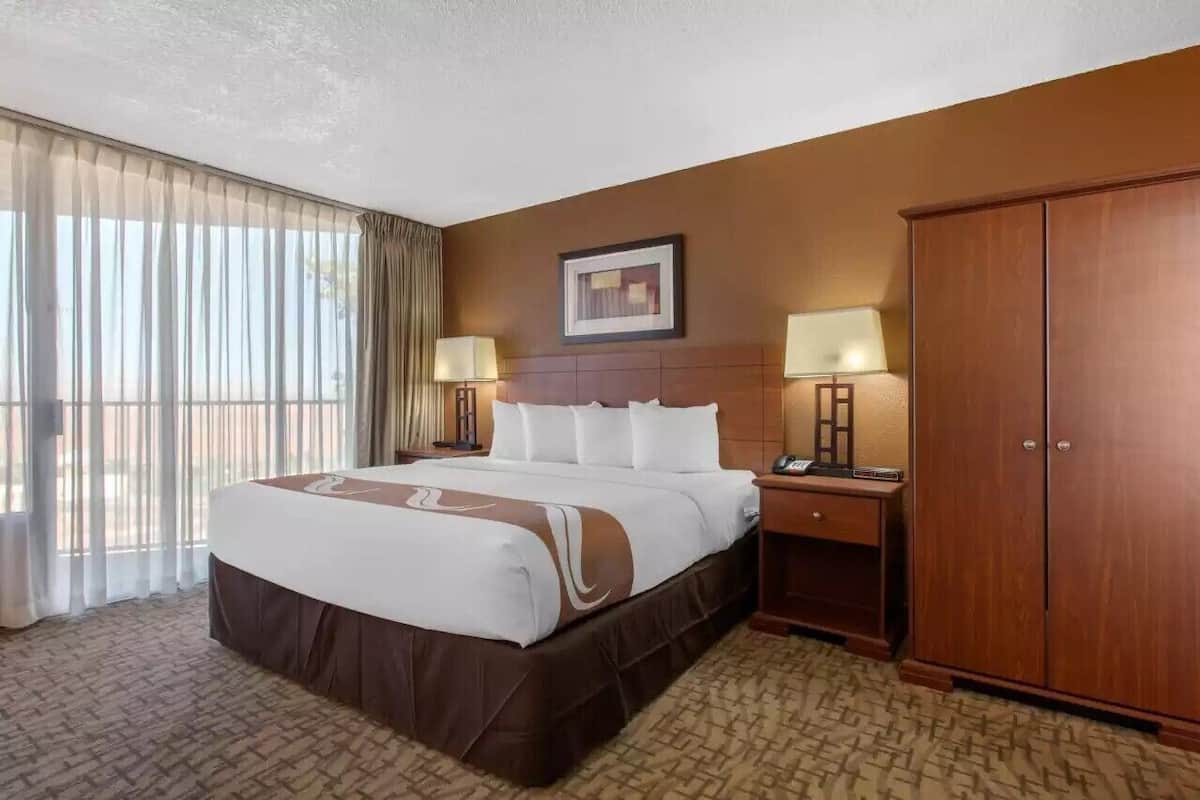 Habitación de hotel con una cama grande, dos mesitas de noche con lámparas, un armario y un cuadro en la pared.