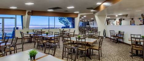 A restaurant with multiple tables and chairs, large windows with a view, and a carpeted floor.