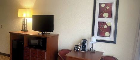 A hotel room with a television on a wooden cabinet, a coffee maker on a table, and two red chairs.