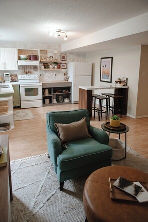 A modern living room with a green armchair, a coffee table, and a kitchen area in the background. - Stylish 3BR Retreat, Prime Local, Sleeps 8+Trundle (Lethbridge)
