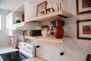 A kitchen with white cabinets, wooden shelves, a stove, and various kitchen items.