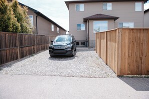 A residential driveway with a parked SUV, a wooden fence, and a two-story house with a visible garage. - Stylish 3BR Retreat, Prime Local, Sleeps 8+Trundle (Lethbridge)