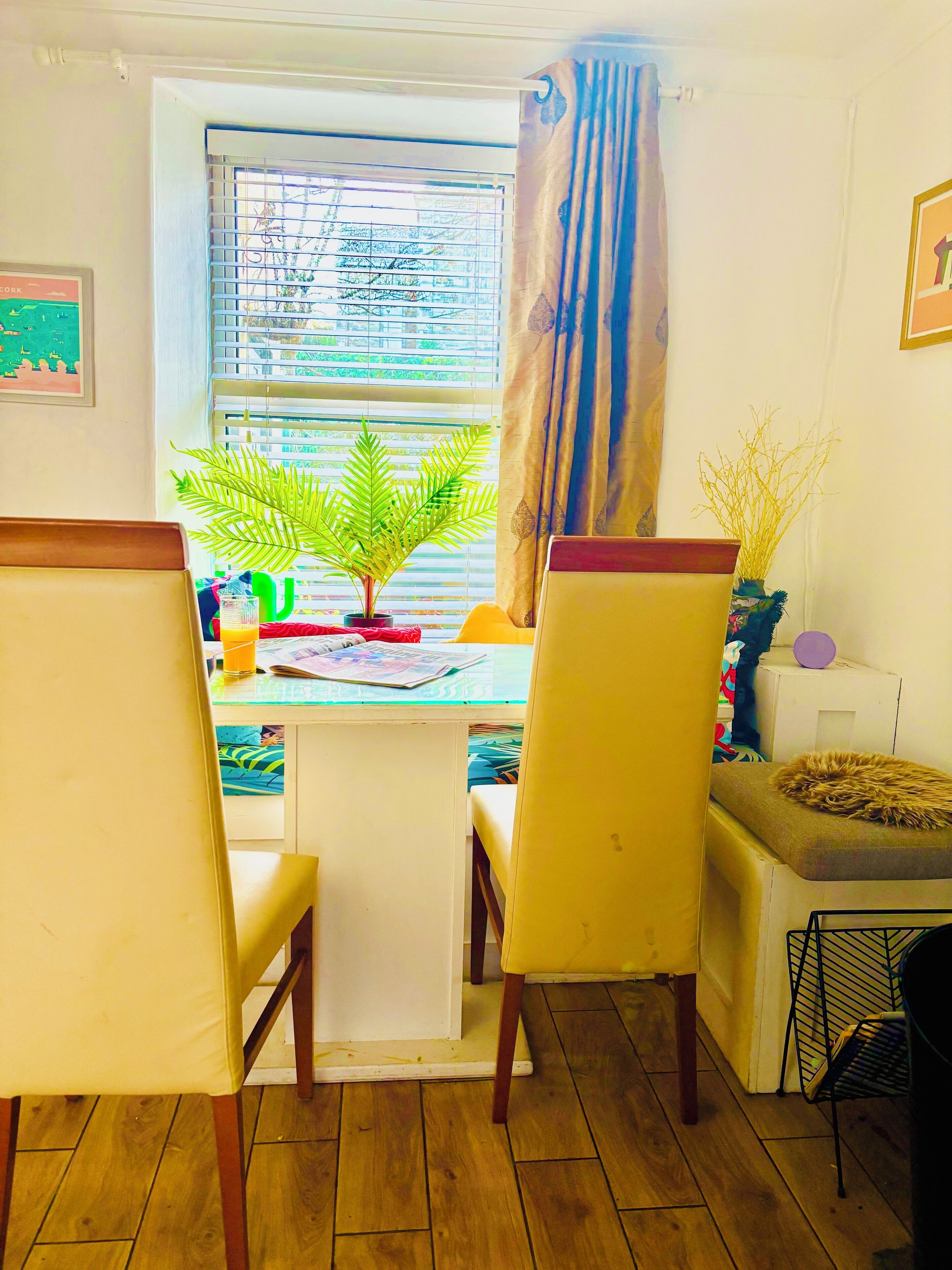 A dining area with a table, chairs, a potted plant, and a window with blinds.