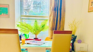 Een eethoek met een tafel, stoelen, een potplant en een raam met jaloezieën.