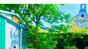 Een patio met een blauw-wit gestreept kussen, een groene metalen tafel en een witte opklapbare stoel.