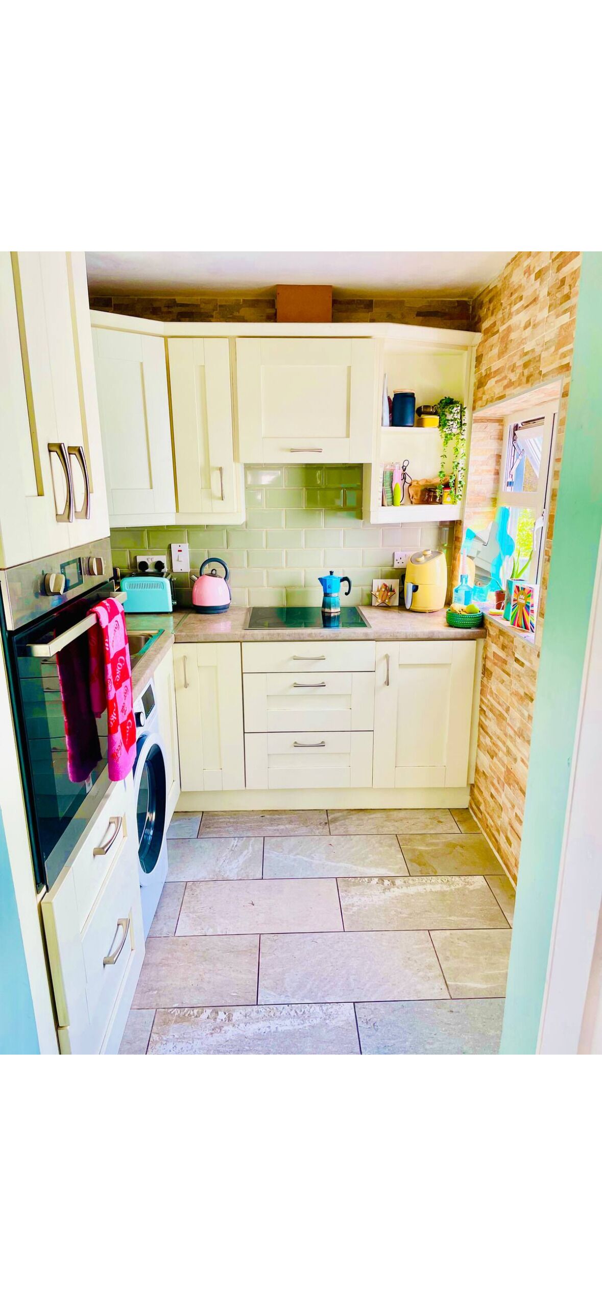 A compact kitchen with light-colored cabinets, a washing machine, a kettle, and a toaster.