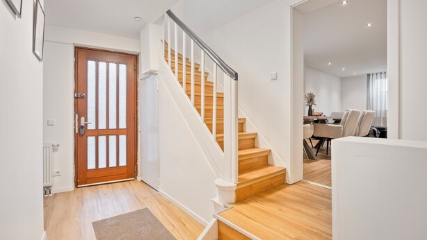 A modern interior with a wooden staircase, a dining area, and a visible door.