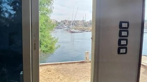 Una habitación con ventana que da a un cuerpo de agua, una zona arenosa y un horizonte urbano distante.