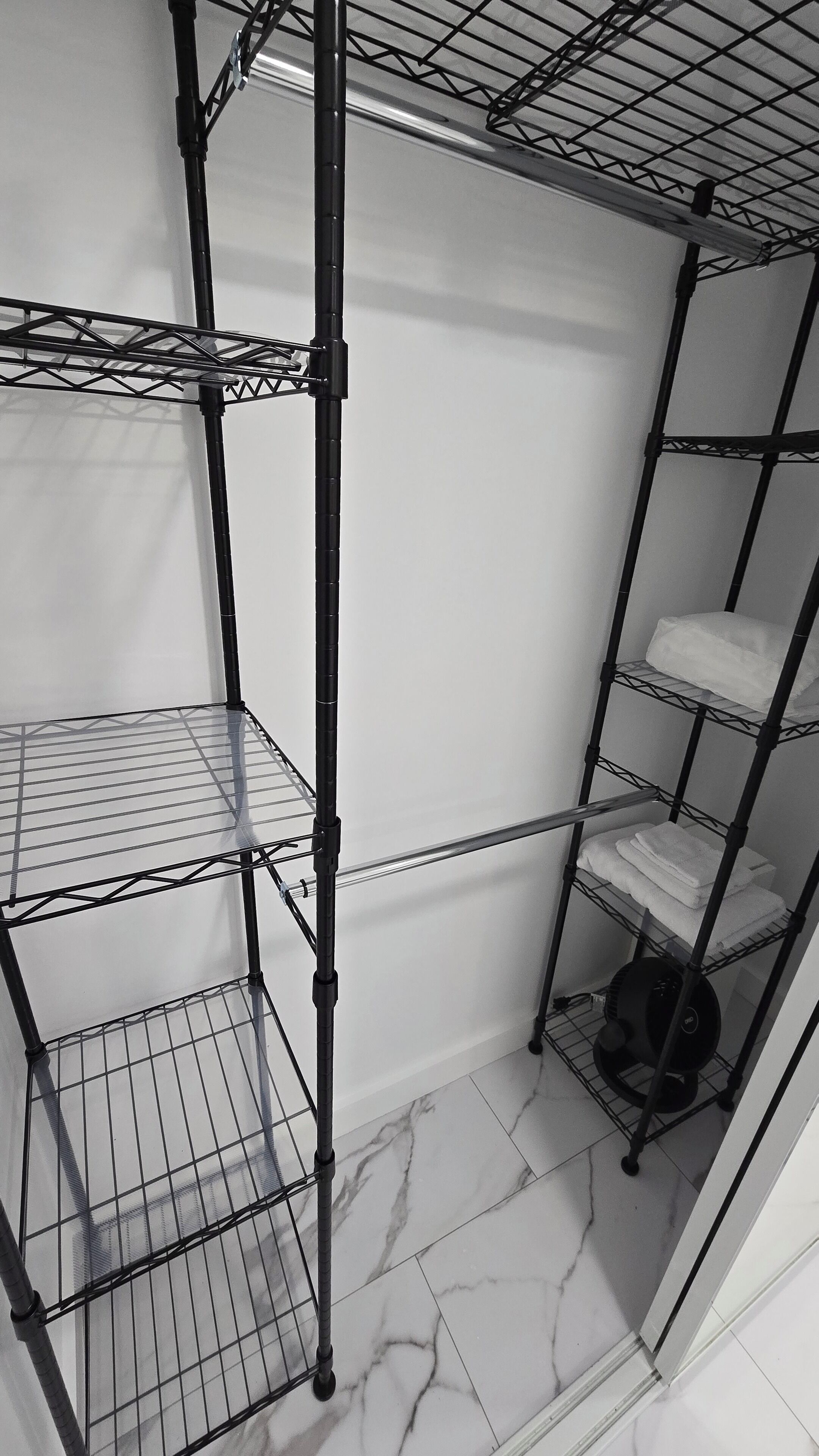 Un espace de rangement doté de plusieurs étagères, d’un ventilateur noir et d’un sol carrelé en marbre.