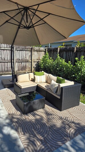 An outdoor patio with a sectional sofa, two side tables, and a large umbrella.