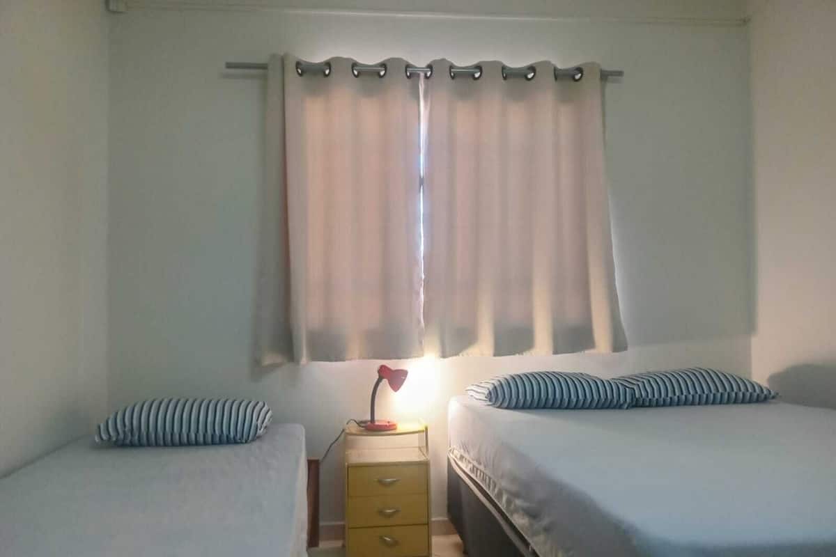 A room with two beds, a nightstand with a lamp, and a window with curtains.
