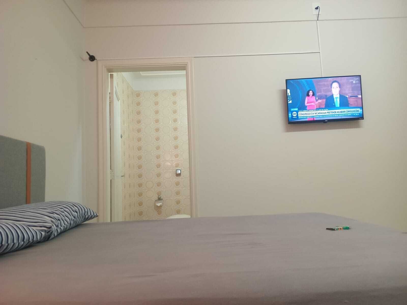 Une pièce comprenant un lit, un téléviseur fixé au mur et une porte donnant sur une autre pièce.