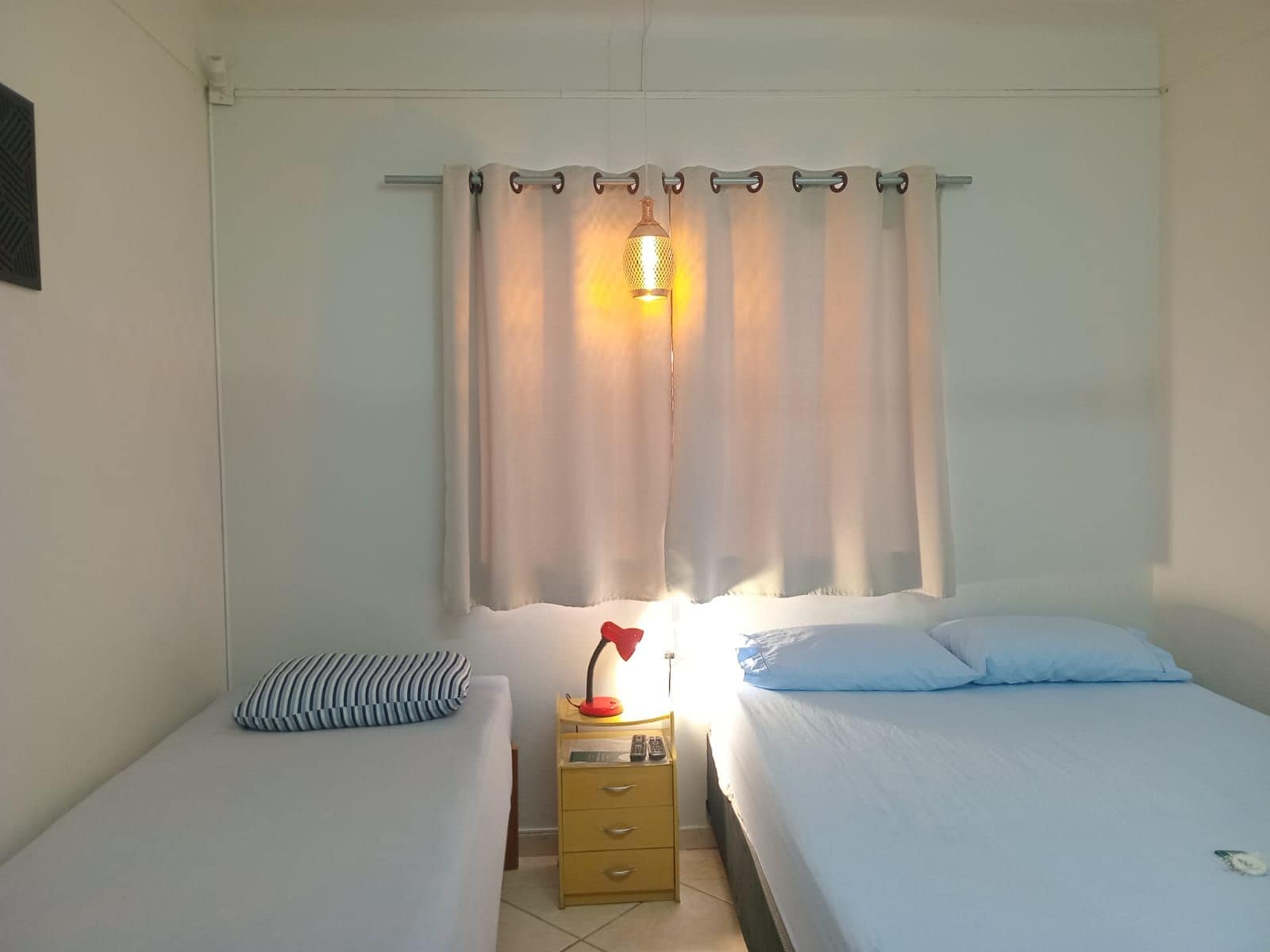 A bedroom with two beds, a nightstand with a lamp, and a window with curtains.