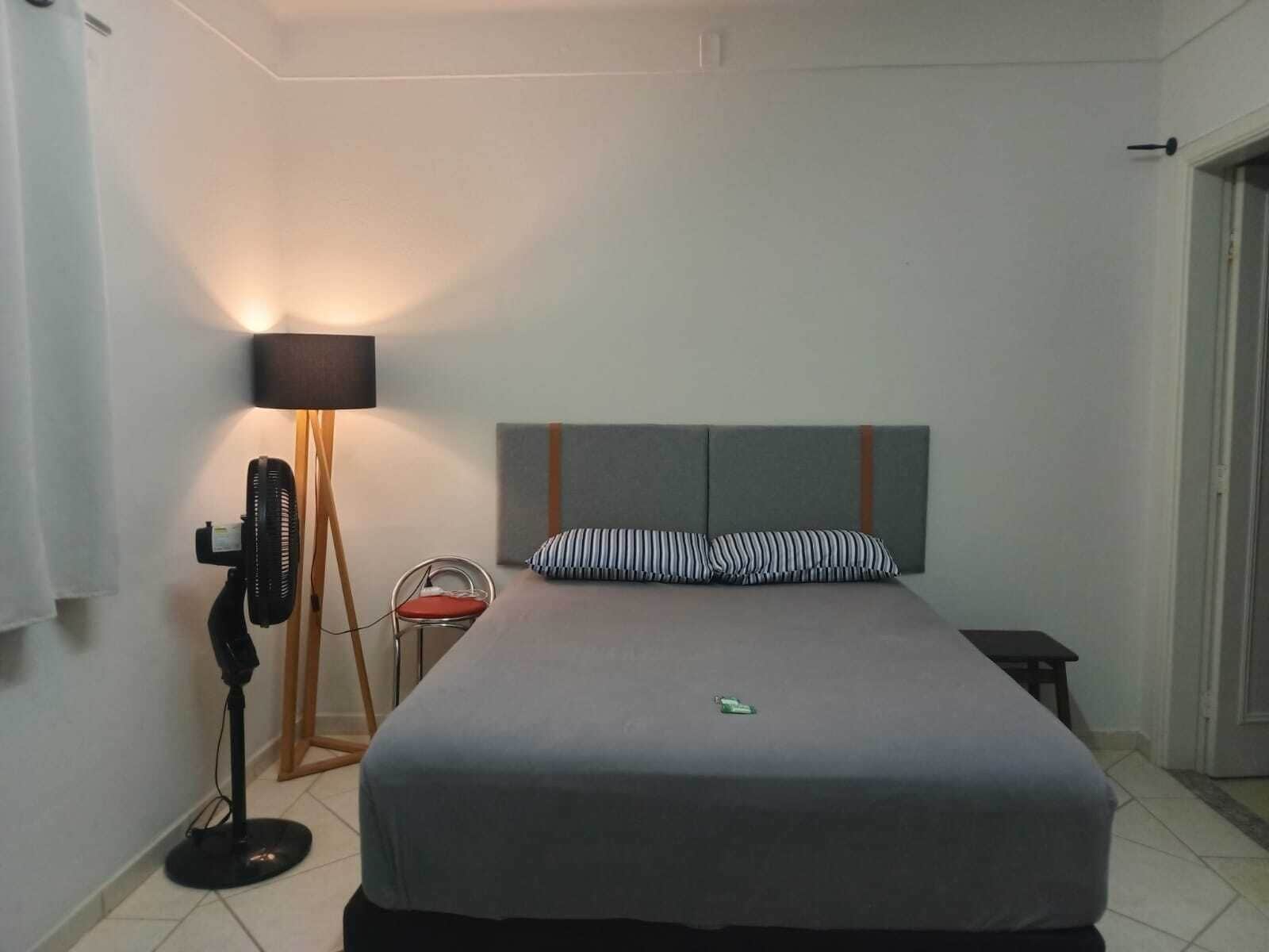 A bedroom with a bed, a bedside table, a lamp, and a chair.