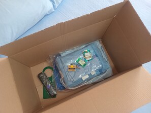 A cardboard box containing a blue towel, a green hair tie, and a remote control. - Capsula Residence Hotel (Marília)