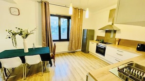 Una cocina compacta con comedor, una ventana con cortinas, un reloj en la pared y una planta sobre la mesa.