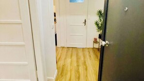 Un pasillo con suelo de madera, puertas blancas y una puerta oscura a la derecha.