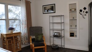 Une pièce comprenant une chaise en bois, un bureau avec une plante, une étagère en métal et un tableau encadré accroché au mur.