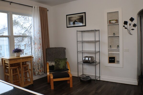 A room with a wooden chair, a desk with a plant, a metal shelving unit, and a framed picture on the wall.