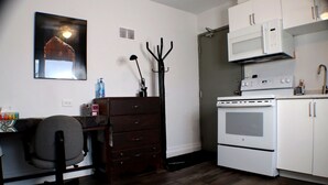 Une cuisine compacte équipée d’un four à micro-ondes, d’une cuisinière et d’un petit coin repas comprenant une chaise et un buffet en bois.