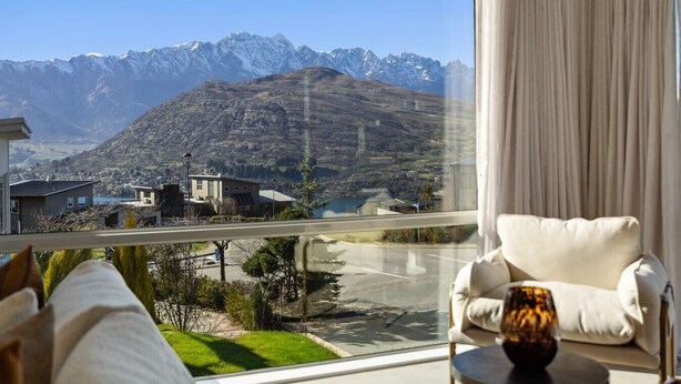 Ein Zimmer mit Blick auf ein Gebirge, ein Sessel und ein Tisch mit einem Glas.