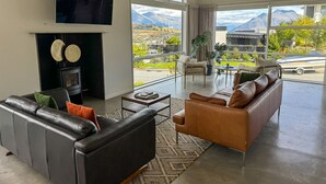 Ein modernes Wohnzimmer mit Kamin, Ledersofas, einem Flachbildfernseher und einem großen Fenster mit Blick auf die Berge.