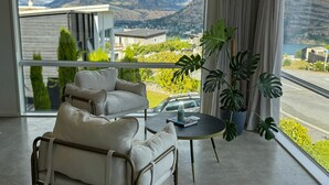 Ein modernes Wohnzimmer mit einer Couch und Sesseln, einem kleinen runden Tisch und großen Fenstern mit Blick auf die Berge.