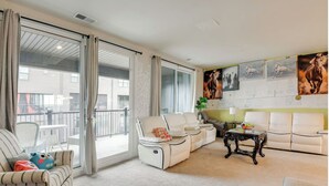 A spacious living room with a white sofa, a white armchair, and a black coffee table. There are large windows with curtains, a balcony, and a wall with horse paintings. - Delightful balti, Washington DC retreat (Laurel)