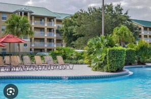 A pool area with lounge chairs, a red umbrella, and a building with balconies in the background. - Magnificent Resot in kissimmee, close to parks and entertainment, FL. (Celebration)