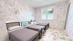 Une chambre avec deux lits, une petite table et une fenêtre avec des stores.
