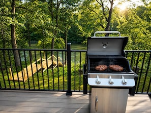 A barbecue grill with two steaks on a deck with a wooden staircase and a metal railing. - The Lakeside Cove 4 Bed 3 Bath near Indiana Beach Full Kitchen Outdoor Firepit (Monticello)