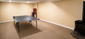 Ein Zimmer mit Tischtennisplatte, Kaminofen und beigem Teppich.