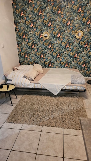 Un dormitorio con una cama, una mesita redonda pequeña, una alfombra y un papel tapiz estampado.