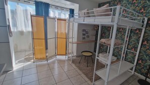 A room with a bunk bed, a small round table, a door with a curtain, and a patterned wall. - A little cocoon in the heart of Cantal (Arpajon-sur-Cère)