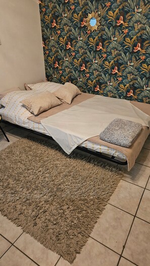 A bed with a patterned headboard, a beige blanket, and a fluffy rug on a tiled floor.