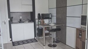 A modern kitchen with white cabinets, a dining area with a table and chairs, and a TV on a stand. - A little cocoon in the heart of Cantal (Arpajon-sur-Cère)