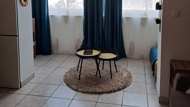 A living room with a view of a cityscape, a round table with two chairs, a sofa, and a decorative wall piece. - A little cocoon in the heart of Cantal (Arpajon-sur-Cère)