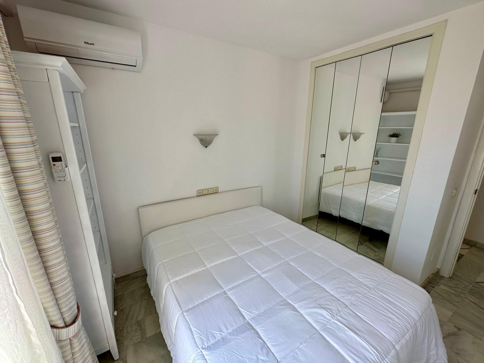 Une chambre à coucher comprenant un lit, une armoire, un miroir et un appareil de climatisation.