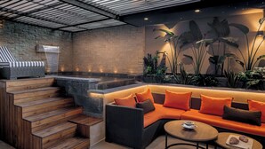 A modern lounge area with a stone wall, a wooden staircase, a black wicker sofa with orange cushions, and a round table with a plate and two croissants. - Oriental chic • 3 bedrooms with private pool and spa (Marrakesh)