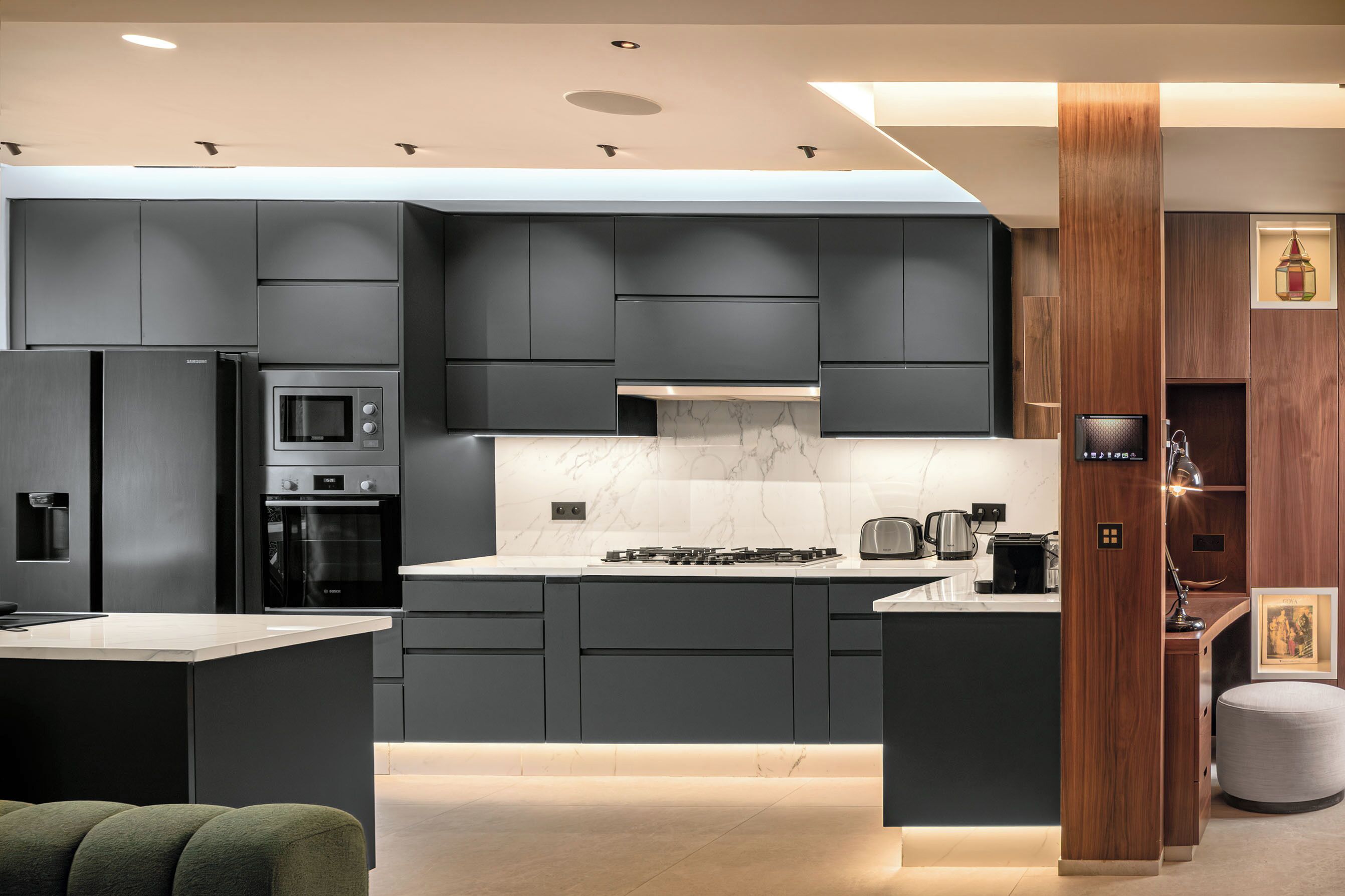 Una cocina moderna con armarios oscuros, una isla central, electrodomésticos integrados y una pared decorativa de madera.